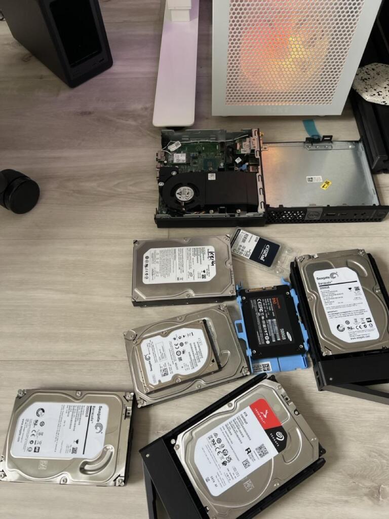 An office floor covered in hard disks, a nas, a open dell optiplex, and a desktop computer.