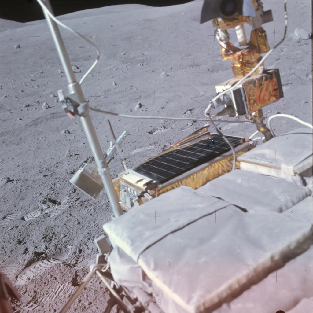 A color photograph of the Apollo 16 lunar rover, centering on some equipment. The object in focus at the center left is a dust brush. Footprints can be seen on the lunar surface behind the rover near the tool’s attachment point, implying the dust brush was recently in use. https://www.nasa.gov/history/alsj/picture.html