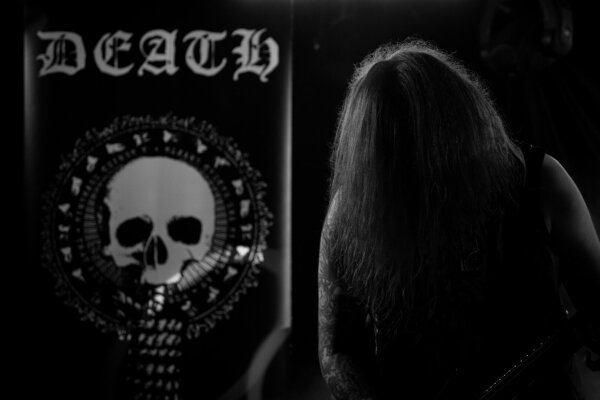 One of the band's backdrops with the word "death" written above a skull. To the left of the image you can just make out the silhouette of one of the bandmembers.